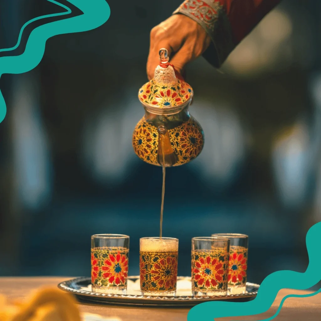 A glass of Moroccan mint tea with fresh mint leaves and sugar cubes on the side.